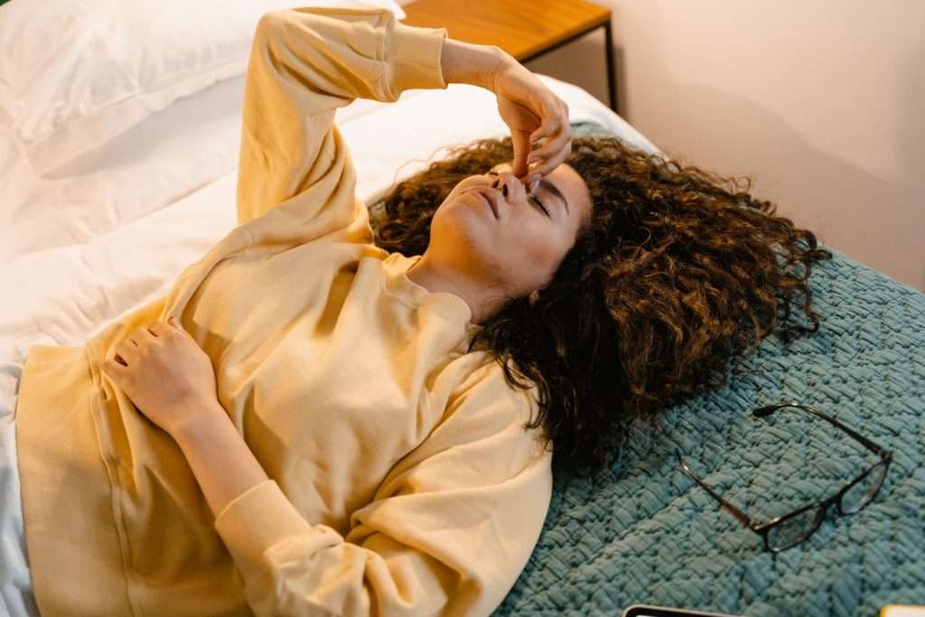 Woman resting in bed with her eyes closed, hand at her temple