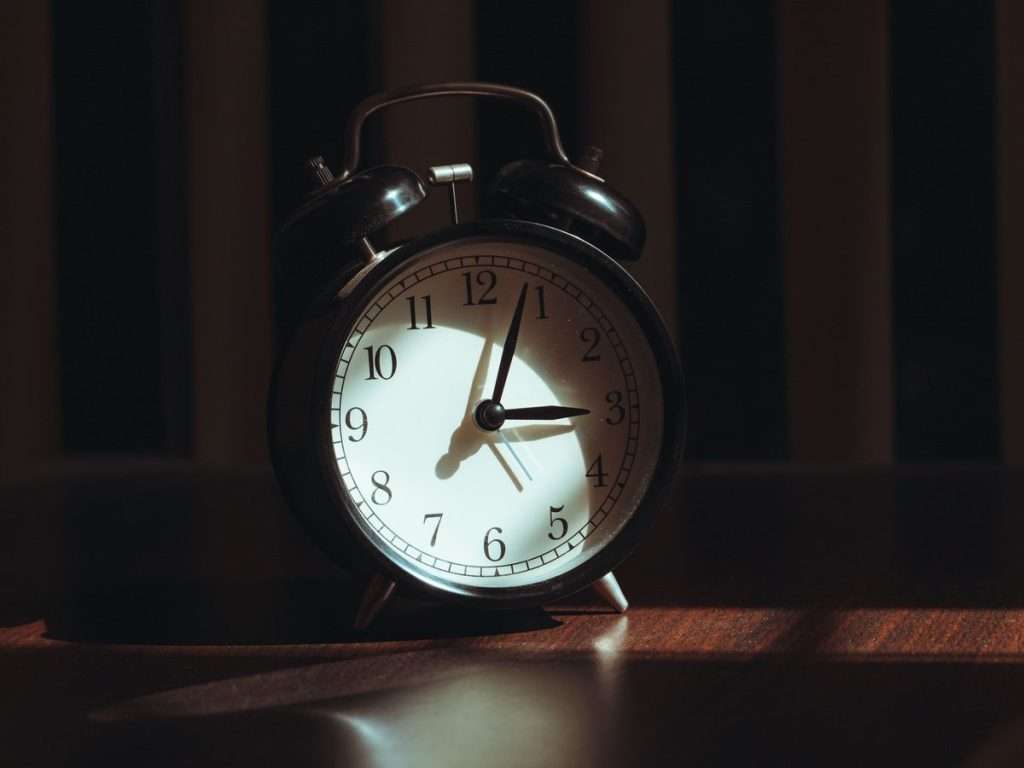 A vintage alarm clock lit by warm light in a dark bedroom, evoking being wide awake at 3am