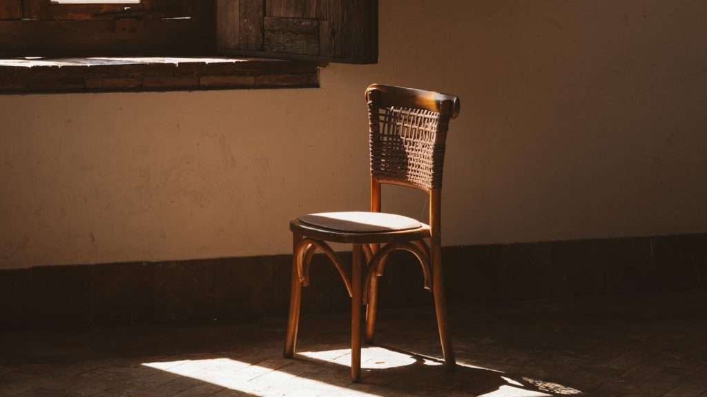 A single empty chair by a window, soft light, a fitting image for grief that hasn't finished its work